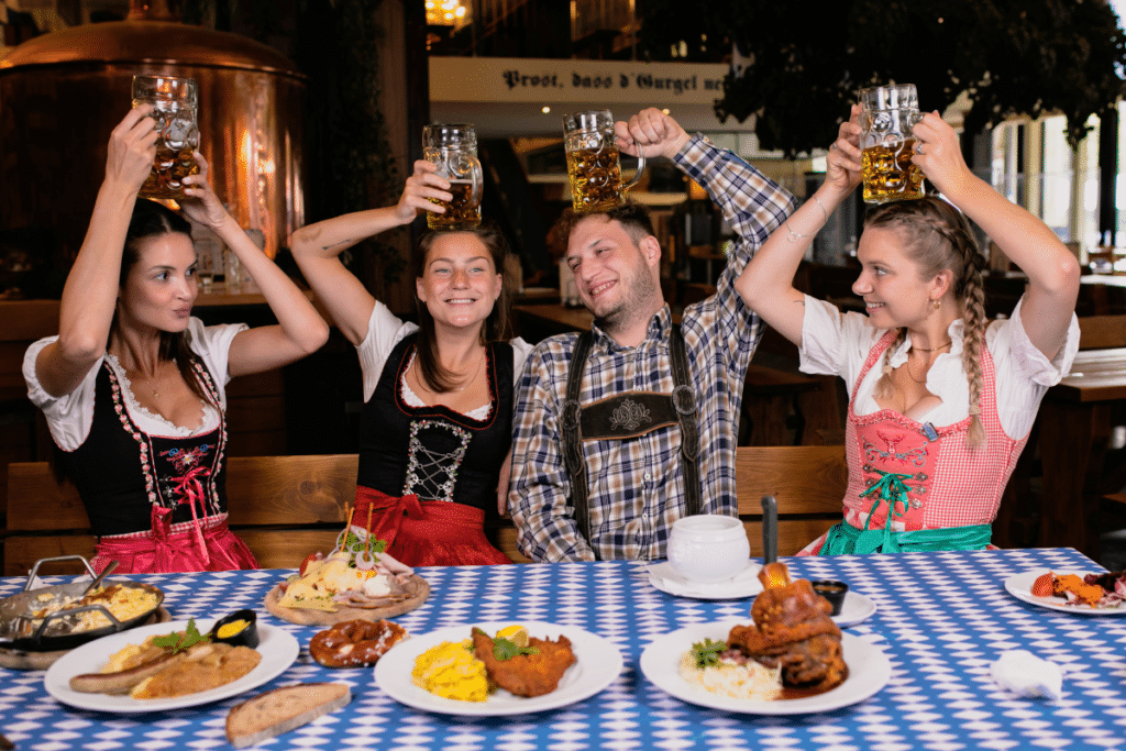 Four people celebrate Oktoberfest with beer, food, and pretzels.